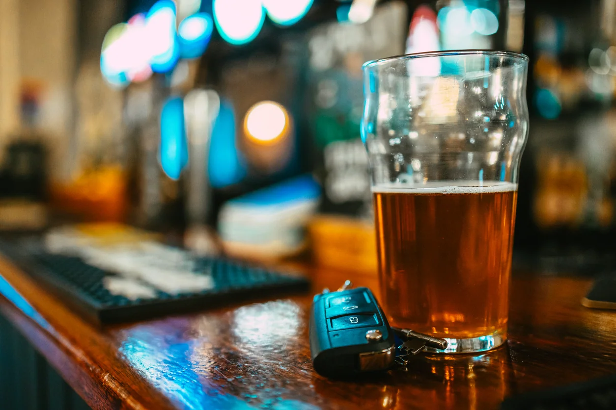 Close up image depicting a partially consumed pint of beer next to a set of car keys on the bar counter, illustrating a drunk driving concepts. Room for copy space.